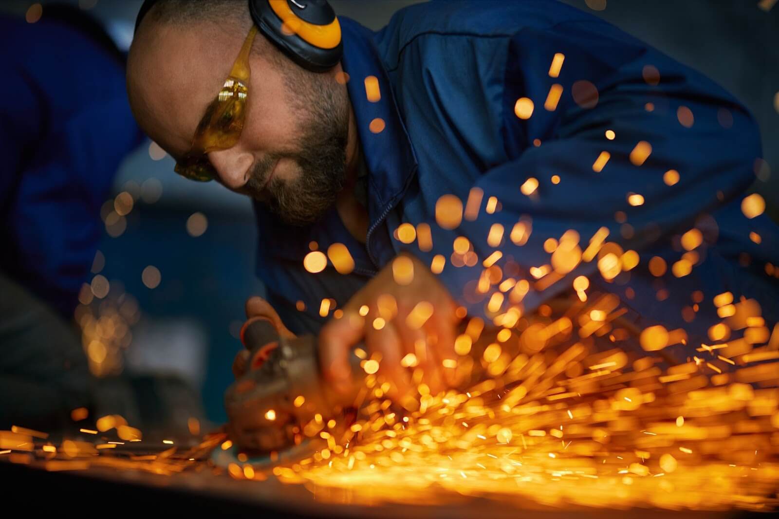 Homem trabalhando com máquina de corte de aço elétrico perto de faíscas